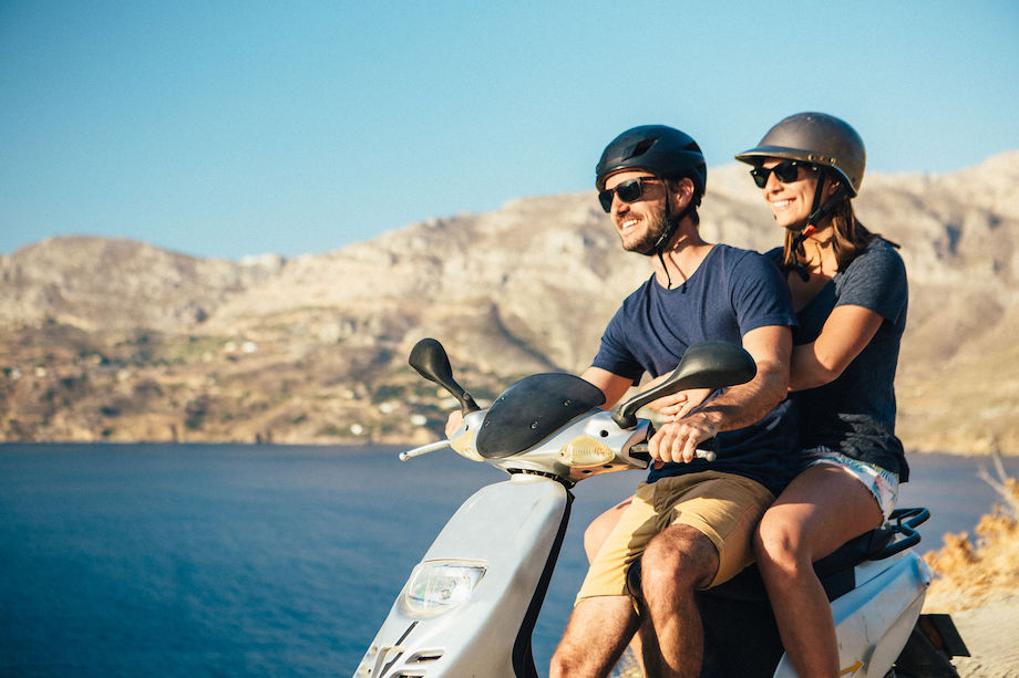 Happy Couple On A Moped Enjoying The View Over The Ocean In Kalymnos, Greece